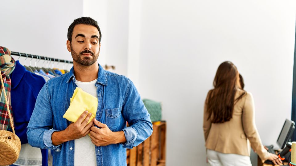 man shopping in retail apparel store concealing unpaid merchandise inside his shirt while retail store associates are not watching