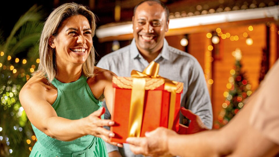 middle-aged male female couple accepting gift package from retailer in holiday themed shopping area