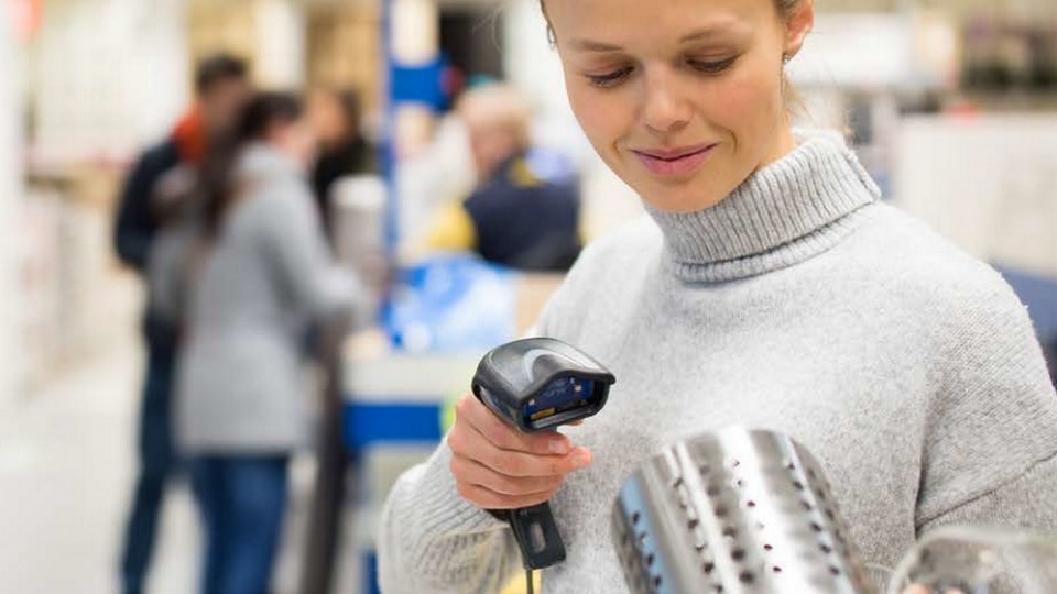 female retail store associate scanning item for purchase with other shoppers in the background