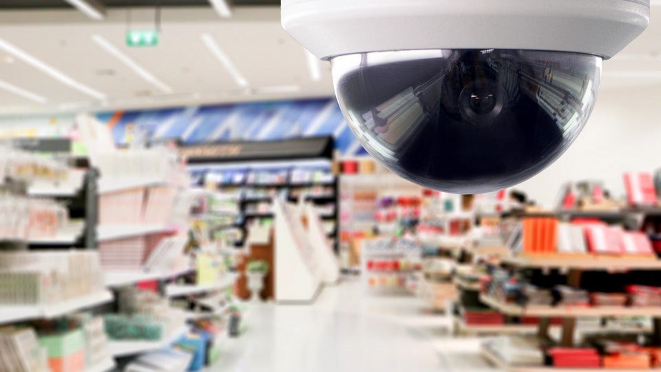 ceiling mounted ip 360 camera in foreground with busy retail store blurred in background