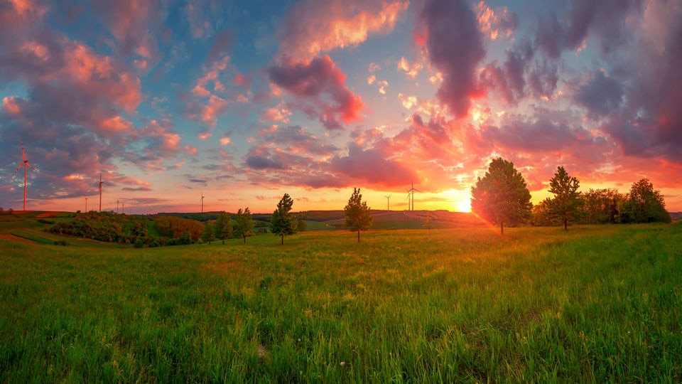 sunset over rural home with lage fields of grass and scattered trees around the house with the sky a deepening blue and rose orange and gold tints to the clouds